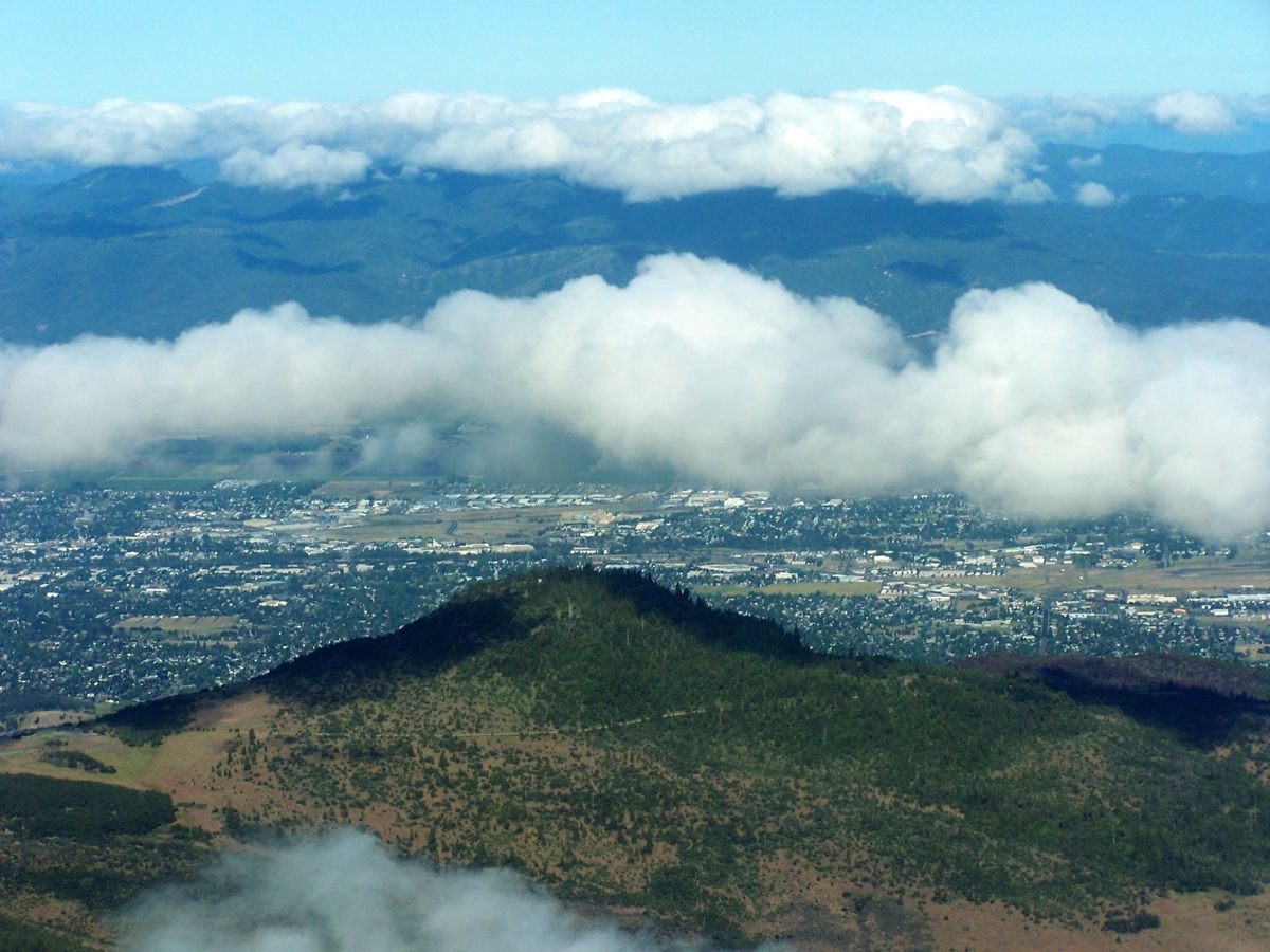Aerial view over Roxy Ann Peak with the city of Medford spread out behind it under clouds